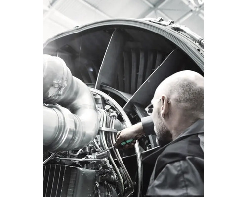 Muž kontroluje a udržuje motor letadla pomocí šroubováku.