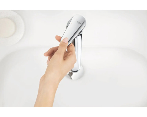 Ruka ovládá chromovanou umyvadlovou baterii od Grohe