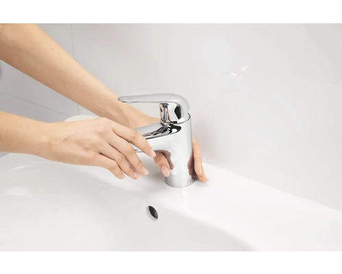 Žena obsluhuje umyvadlovou baterii v koupelnovém umyvadle.