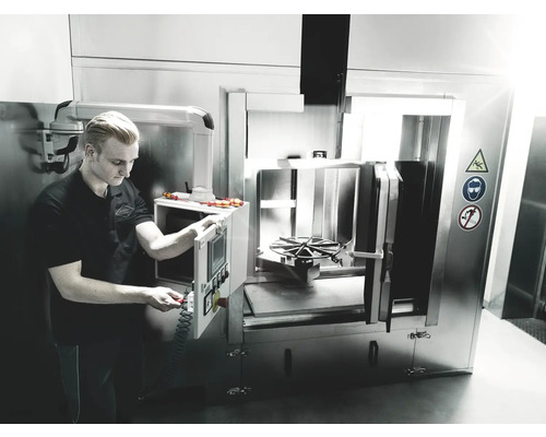 Zaměstnanec obsluhuje ocelové čisticí zařízení ve výrobní hale.