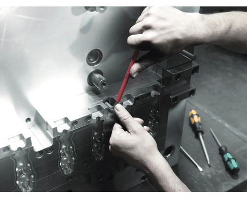 Pracovník provádí údržbu kovového nástroje pomocí šroubováku.