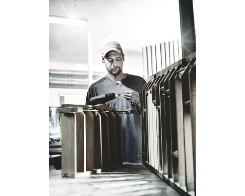 Řemeslník pracuje s akumulátorovou vrtačkou na dřevěném objektu v dílně.