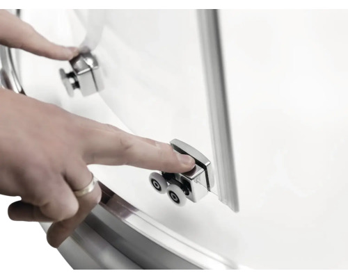 Detailní záběr dveří sprchového koutu s válečkovým mechanismem a rukou, která se jich dotýká