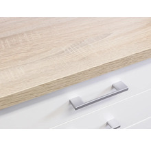 Detail komody se světle hnědou dřevěnou deskou a bílými zásuvkami se stříbrnými úchyty.