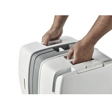 Dvě ruce zvedají přenosnou kočičí toaletu za držadlo.