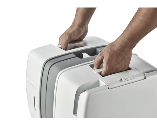 Dvě ruce zvedají přenosnou kočičí toaletu za držadlo.