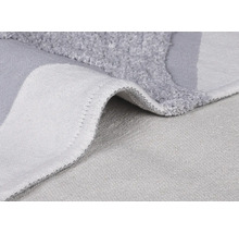 Detail šedé koupelnové předložky s vlasem a tkanou zadní stranou.