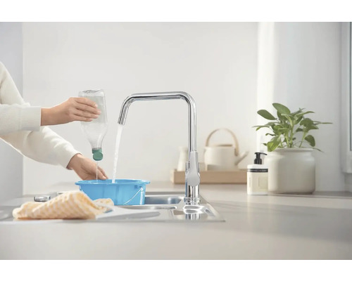 Osoba nalévá vodu z láhve do modré misky pod kohoutkem