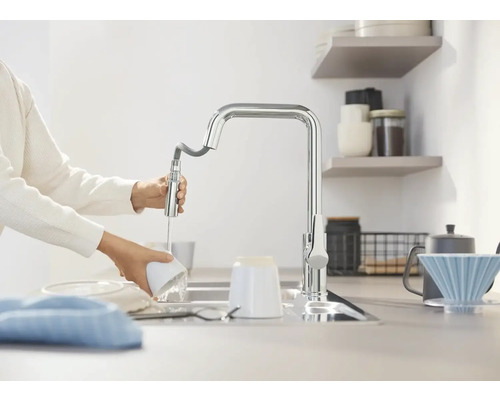 Osoba myje nádobí s kuchyňskou baterií.
