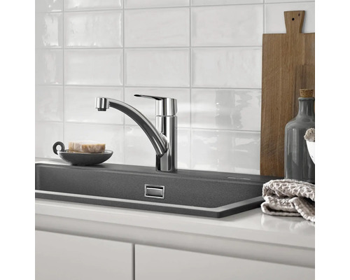 Kuchyňská scéna s dřezovou baterií, dřezem a kuchyňskými potřebami.