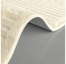 Detail světlého koberce s tkanou texturou a stočeným rohem, který ukazuje spodní stranu