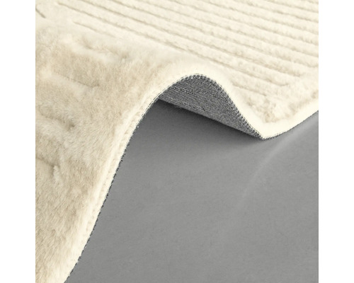 Detail světlého koberce s tkanou texturou a stočeným rohem, který ukazuje spodní stranu