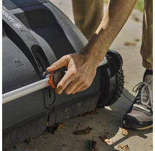 Osoba obsluhuje zametač trávníku s nastavitelnou rukojetí.