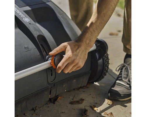 Osoba obsluhuje zametač trávníku s nastavitelnou rukojetí.