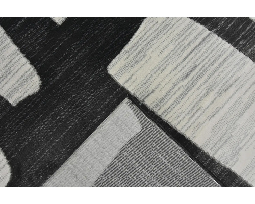 Detailní záběr na tkaný koberec s geometrickým vzorem v černé, šedé a bílé barvě se strukturovaným povrchem.
