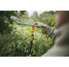 Zahradní scéna s osobou připevňující vějířové hrábě k násadě.