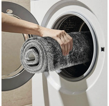 Osoba vkládá šedý koupelnový kobereček do pračky.