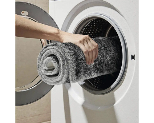 Osoba vkládá srolovaný, pratelný koberec do pračky.