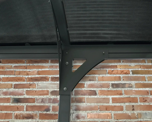 Detailní pohled na zahradní pavilon s polykarbonátovou střechou a podpůrnou konstrukcí u cihlové zdi