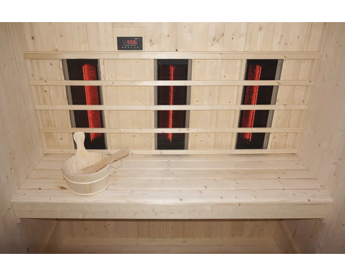 Interiér sauny s infračervenými zářiči, dřevěnými lavicemi a dřevěným vědrem s naběračkou.