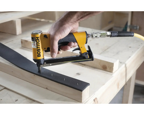 Logo společnosti Bostitch na pneumatické hřebíkovačce používané na dřevěném trámu