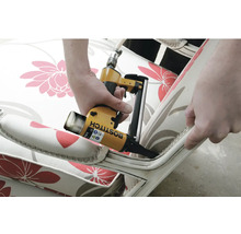 Detailní záběr osoby používající pneumatickou sešívačku k připevnění látky na nábytek.