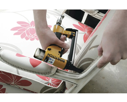 Detailní záběr osoby používající pneumatickou sešívačku k připevnění látky na nábytek.