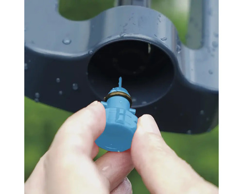 Detailní záběr ruky vkládající trysku do zavlažovače trávníku.