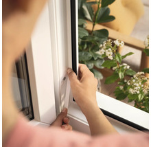 Osoba montuje okenní těsnění na bílý rám okna.