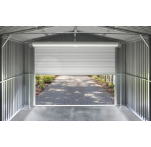 Vnitřní pohled na kovový domek na nářadí se stěnami z vlnitého plechu a pootevřenými rolovacími vraty s výhledem na dlážděnou cestu.