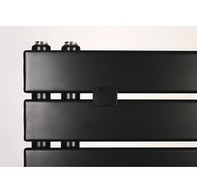 Detailní záběr na matně černý radiátor s plochými panely a vertikálními přípojkami.