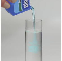 Modrá kapalina se nalévá z láhve do zkumavky naplněné vodou pro ukázku procesu míchání.