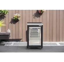 Mobilní venkovní chladnička Tenneker s prosklenými dveřmi a kolečky na terase před dřevěnou stěnou.