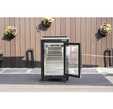 Černá venkovní chladnička Tenneker s otevřenými prosklenými dveřmi a kovovými policemi na terase před plotem.