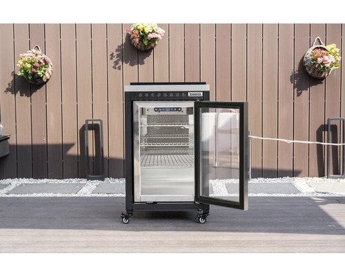 Černá venkovní chladnička Tenneker s otevřenými prosklenými dveřmi a kovovými policemi na terase před plotem.