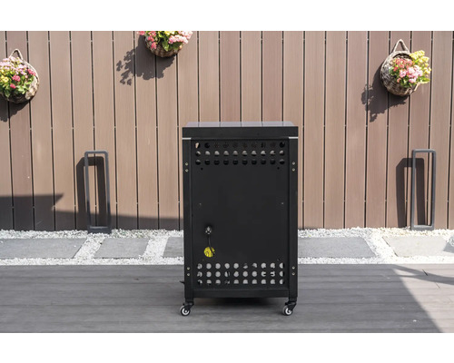 Mobilní spodní skříňka venkovní kuchyně v černé barvě s větracími otvory a elektrickou přípojkou na terase před dřevěným plotem.