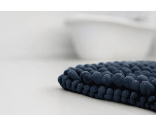 Tmavě modrá koupelnová předložka s žinylkovou strukturou před vanou.
