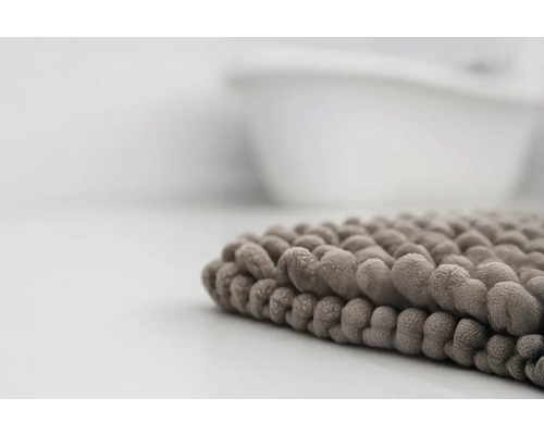 Detailní pohled na měkkou koupelnovou předložku s žinylkovou strukturou u vany.