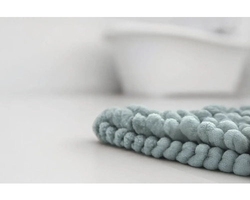 Detailní záběr na měkkou koupelnovou předložku z mikrovlákna s žinylkovou strukturou v koupelně před vanou.