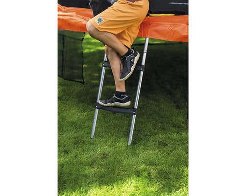 Kovový žebřík k trampolíně se dvěma plastovými stupni, připevněný k trampolíně na zahradě.