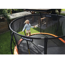 Dítě skáče na kulaté zahradní trampolíně Marimex s černou ochrannou sítí a oranžovým krytem pružin na zahradě.