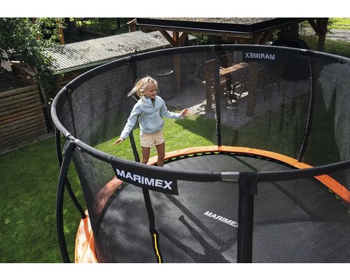 Dítě skáče na kulaté zahradní trampolíně Marimex s černou ochrannou sítí a oranžovým krytem pružin na zahradě.