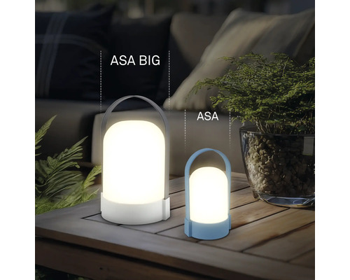 Dvě moderní LED lucerny ASA BIG a ASA na dřevěném stole, atmosférické venkovní osvětlení s rostlinami a pohovkou v pozadí.