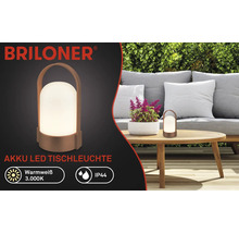 Briloner Logo, akumulátorová LED stolní lampa na dřevěném stole v zahradě s pohovkou a plotem, teplá bílá 3000 Kelvinů, krytí IP44.