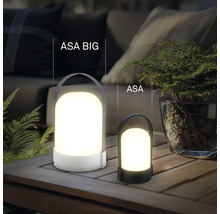 Dvě různě velké přenosné LED stolní lampy ASA BIG a ASA na dřevěném stole venku s rostlinami a čalouněným nábytkem.
