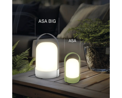 Dvě moderní přenosné LED stolní lampy ASA BIG a ASA z plastu na dřevěném stole ve světlém, organizovaném venkovním prostoru.