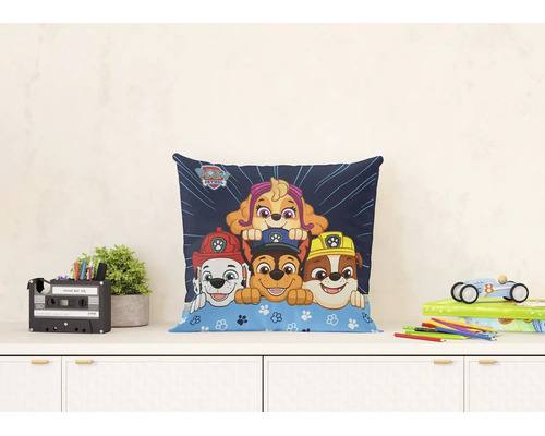 Dekorační polštář Paw Patrol s motivy postav Marshall, Chase, Rubble a Skye na komodě v dětském pokoji.