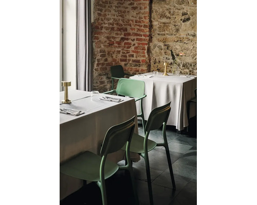 Moderní zelené plastové židle s područkami u prostřených stolů v organizované restauraci s rustikálními cihlovými zdmi.