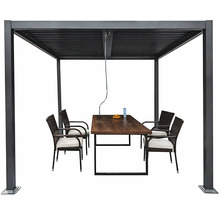 Kovová pergola s lamelovou střechou a klikou, pod kterou stojí dřevěný zahradní stůl a čtyři ratanové židle s podsedáky.