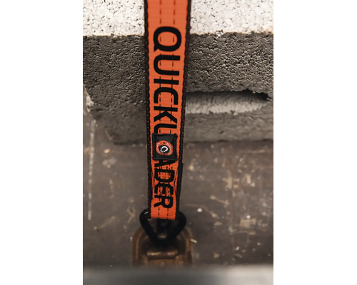 Detail oranžového upínacího popruhu Quickloader s černým nápisem a kovovým hákem.